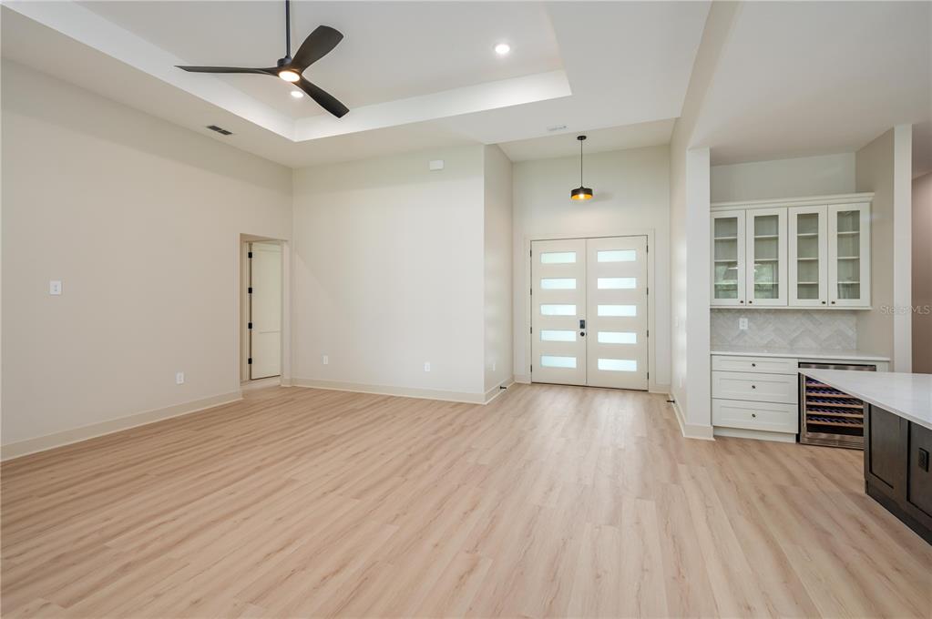 A bright, open-concept room features light wood flooring, a tray ceiling, and a wet bar — 5410 PARKER ESTATES LOOP, LAKELAND, FL