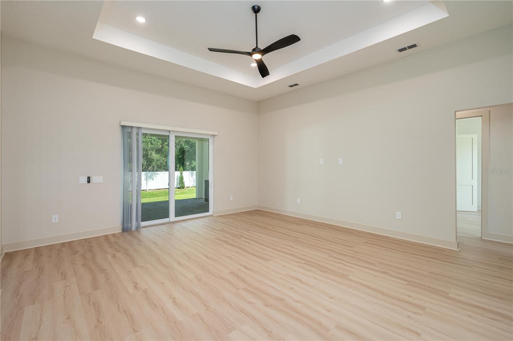 An empty living room features a tray ceiling, a ceiling fan, and sliding glass doors — 5410 PARKER ESTATES LOOP, LAKELAND, FL