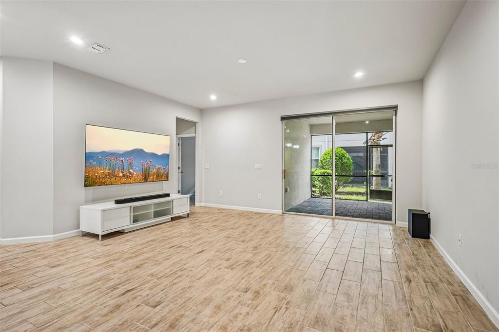 A living room with light wood-look tile floors, a wall-mounted television, and sliding glass doors — 19405 MONARCH WIND WAY, LUTZ, FL