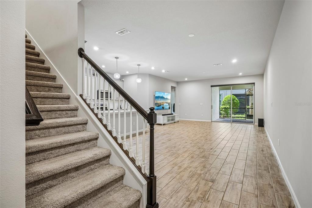 A carpeted staircase leads down to an open-concept living area with tile flooring and sliding doors — 19405 MONARCH WIND WAY, LUTZ, FL