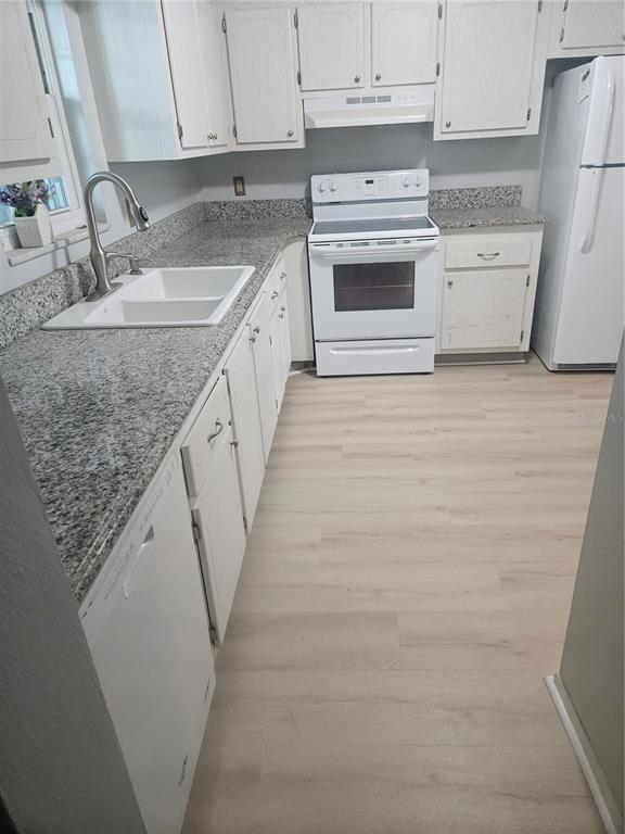 A kitchen featuring white cabinets, granite countertops, a white stove, and light wood-look flooring — 1706 BELLEAIR FOREST DRIVE UNIT 310, BELLEAIR, FL