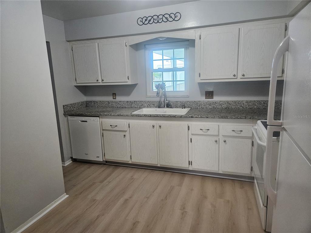A kitchen features white cabinets, granite countertops, a white sink, and light wood-look flooring — 1706 BELLEAIR FOREST DRIVE UNIT 310, BELLEAIR, FL
