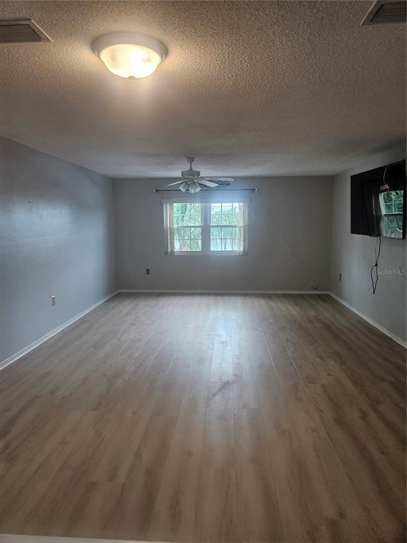 An empty living room features light wood-look flooring, gray walls, a ceiling fan, and a window — 1706 BELLEAIR FOREST DRIVE UNIT 310, BELLEAIR, FL