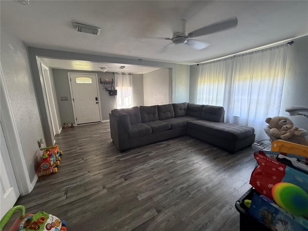 A living room features gray wood-look flooring, a large sectional sofa, and a ceiling fan — 4233 OLD US HIGHWAY 41, RUSKIN, FL