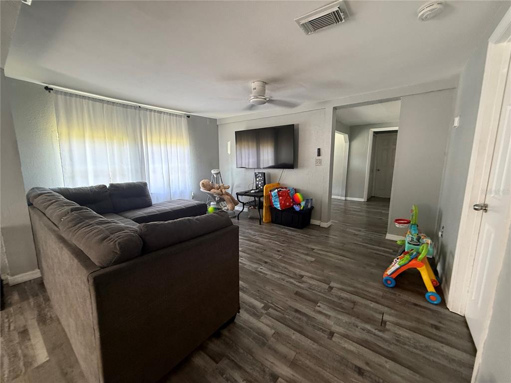 A living room features a grey sectional sofa, wood-look flooring, and a wall-mounted television — 4233 OLD US HIGHWAY 41, RUSKIN, FL