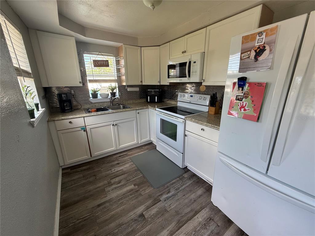 A kitchen features white cabinets, stainless steel appliances, granite countertops, and wood-look flooring — 4233 OLD US HIGHWAY 41, RUSKIN, FL