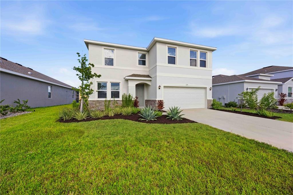 A two-story suburban house with a white stucco exterior, stone accents, and a two-car garage — 624 160TH STREET E, BRADENTON, FL
