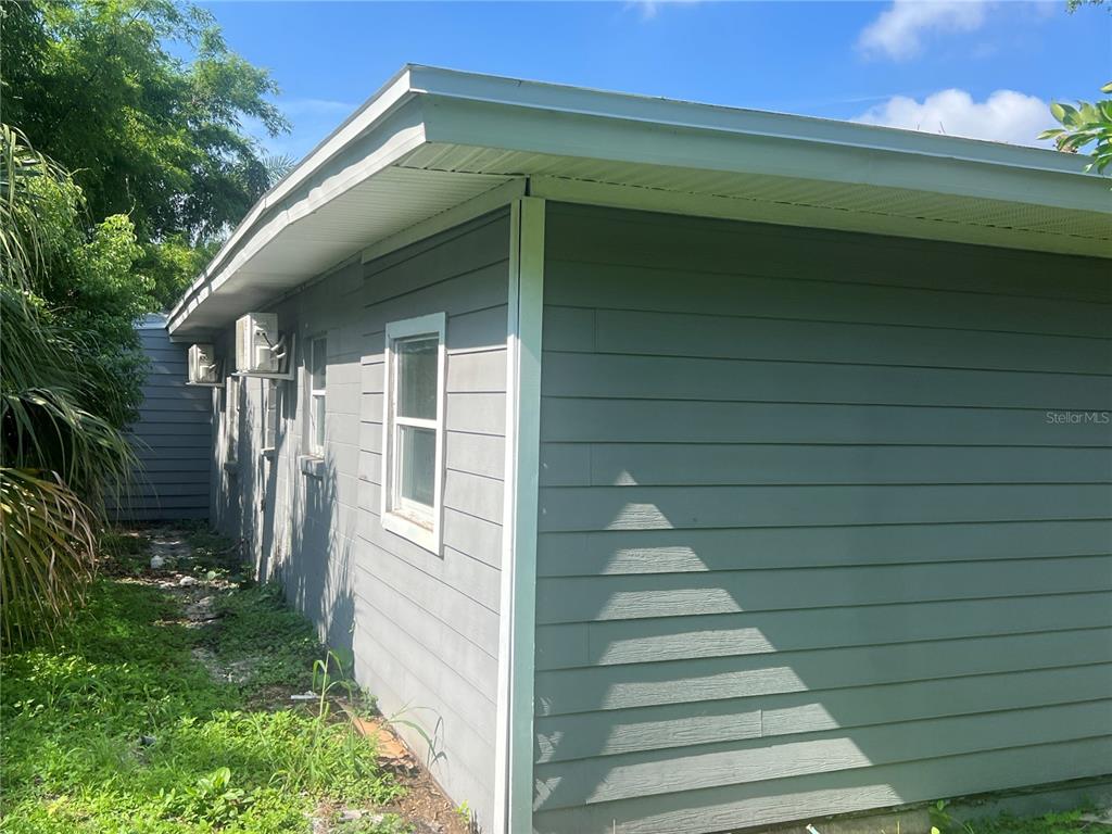 The exterior of a grey, horizontal-sided house features a white-trimmed window and wall-mounted air conditioners — 2002 E 33RD AVENUE, TAMPA, FL
