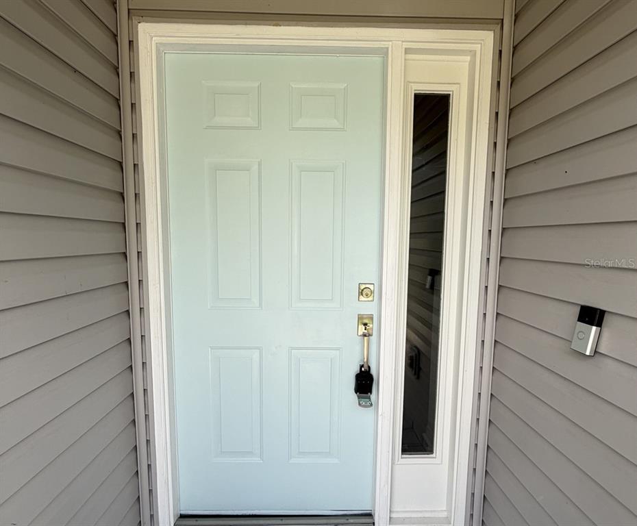 A light blue front door with a side window and a smart doorbell on gray siding — 29204 PRINCEVILLE DRIVE, SAN ANTONIO, FL