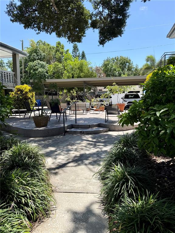 A concrete patio features outdoor seating and a covered parking area under a large tree — 450 32ND AVE N UNIT 107W, ST PETERSBURG, FL