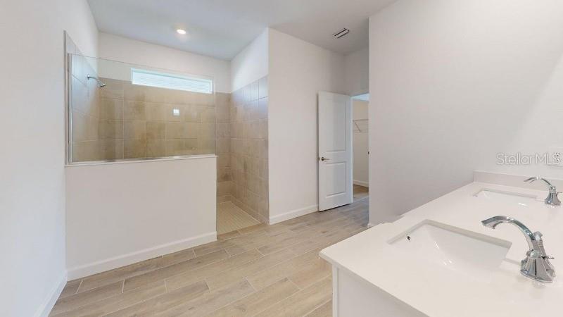 A bathroom features a double vanity with white countertops and a walk-in tiled shower — 7761 LAKES EDGE LANE, PORT CHARLOTTE, FL