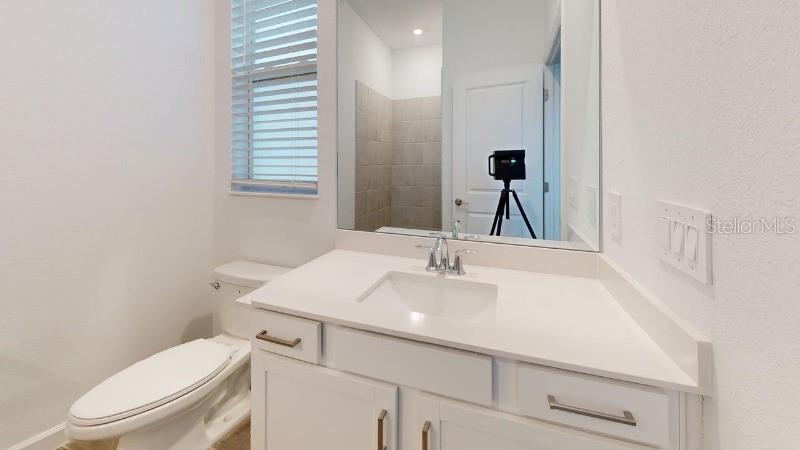 A bathroom features a white vanity with a quartz countertop, a mirror, and a toilet — 7761 LAKES EDGE LANE, PORT CHARLOTTE, FL