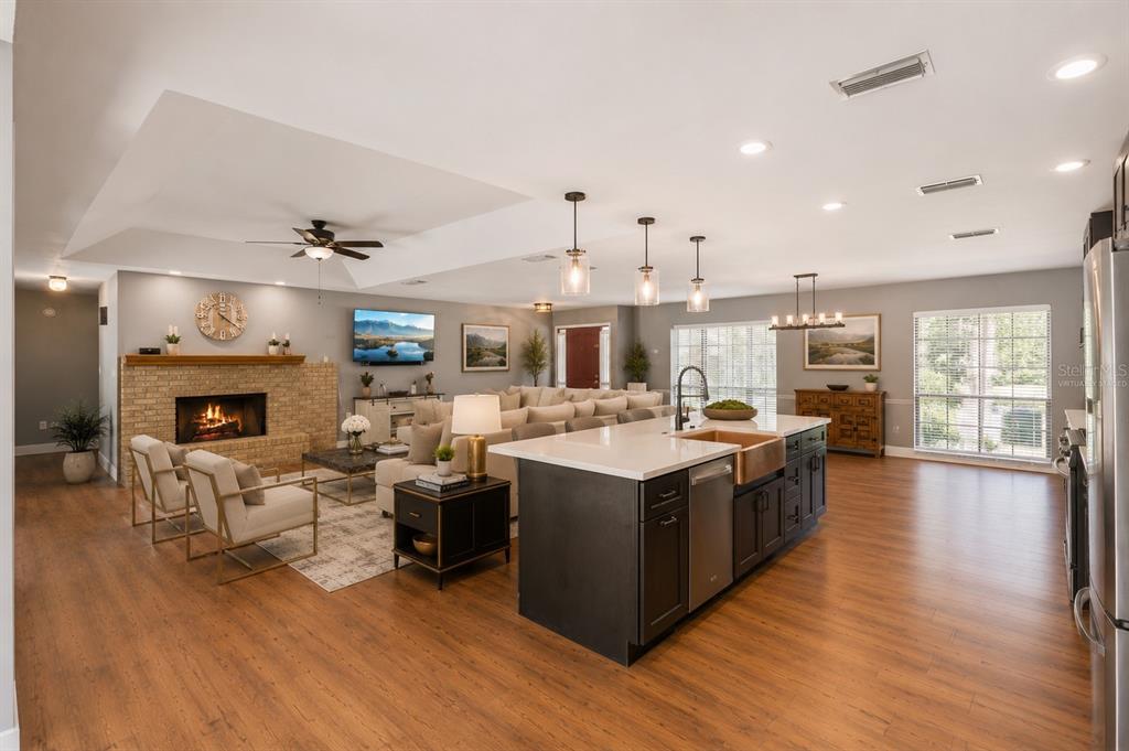 An open-concept living room and kitchen featuring a brick fireplace, large island, and wood flooring — 432 BURNT TREE LANE, APOPKA, FL