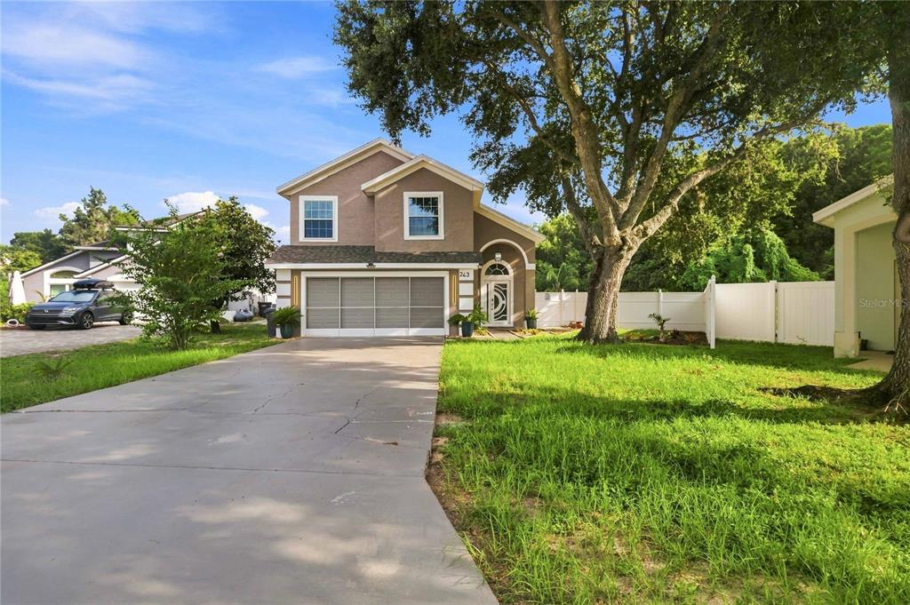 A two-story house with a concrete driveway, a garage, and a large tree in front — 243 OXFORD ROAD, DAVENPORT, FL