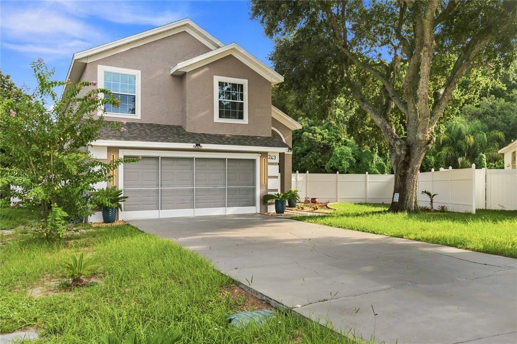 A two-story house with a gray garage door, a concrete driveway, and a white fence — 243 OXFORD ROAD, DAVENPORT, FL