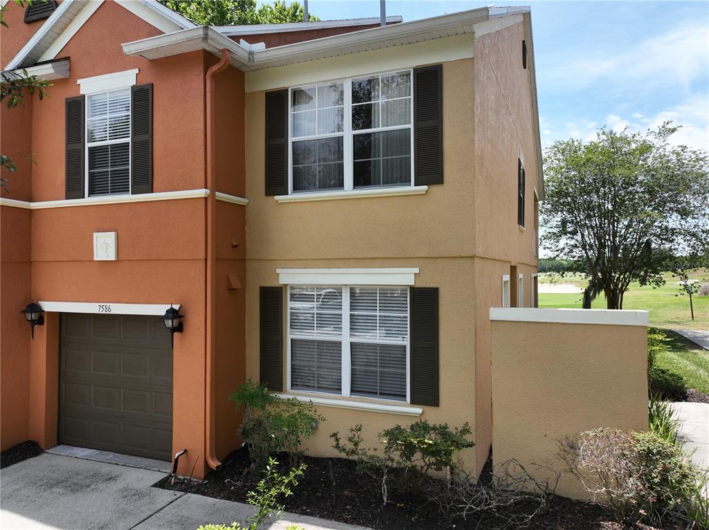 A two-story orange townhouse with a brown garage door and dark shutters — 7586 ASSEMBLY LANE, REUNION, FL