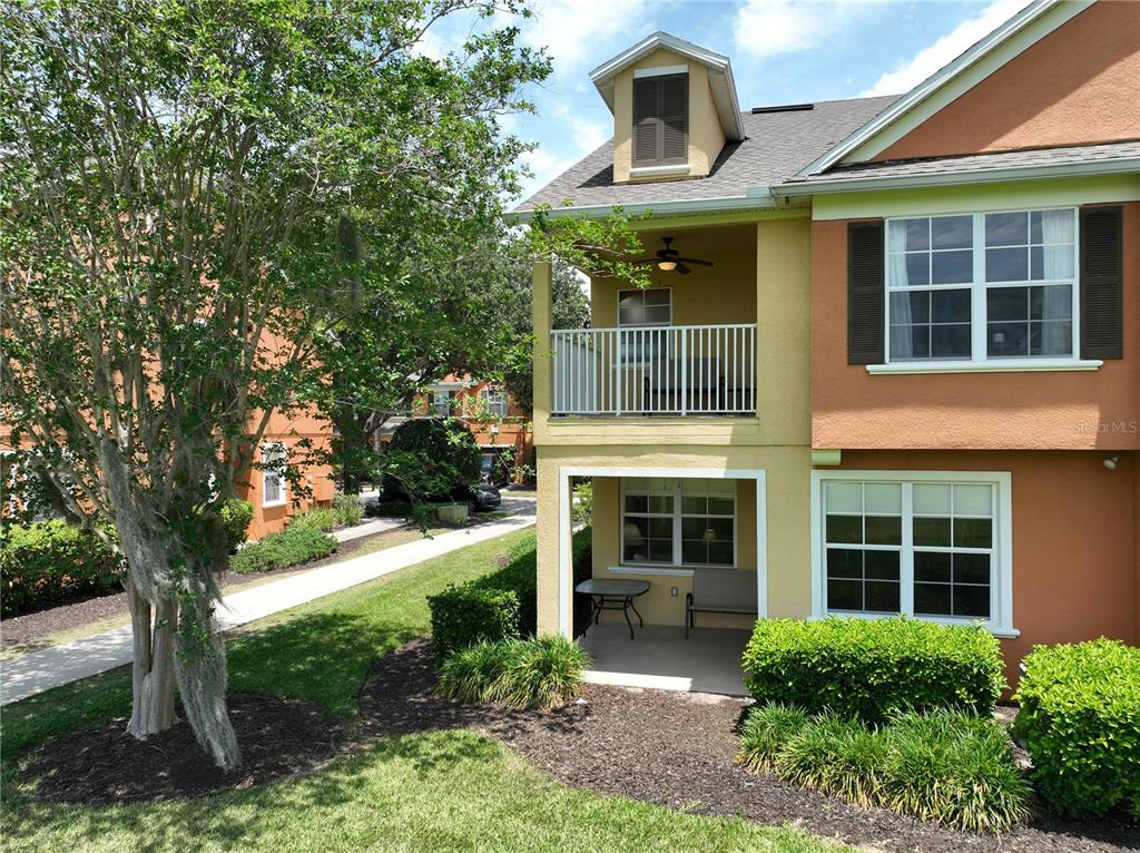 An exterior view of a two-story townhouse with a balcony, patio, and landscaped yard — 7586 ASSEMBLY LANE, REUNION, FL