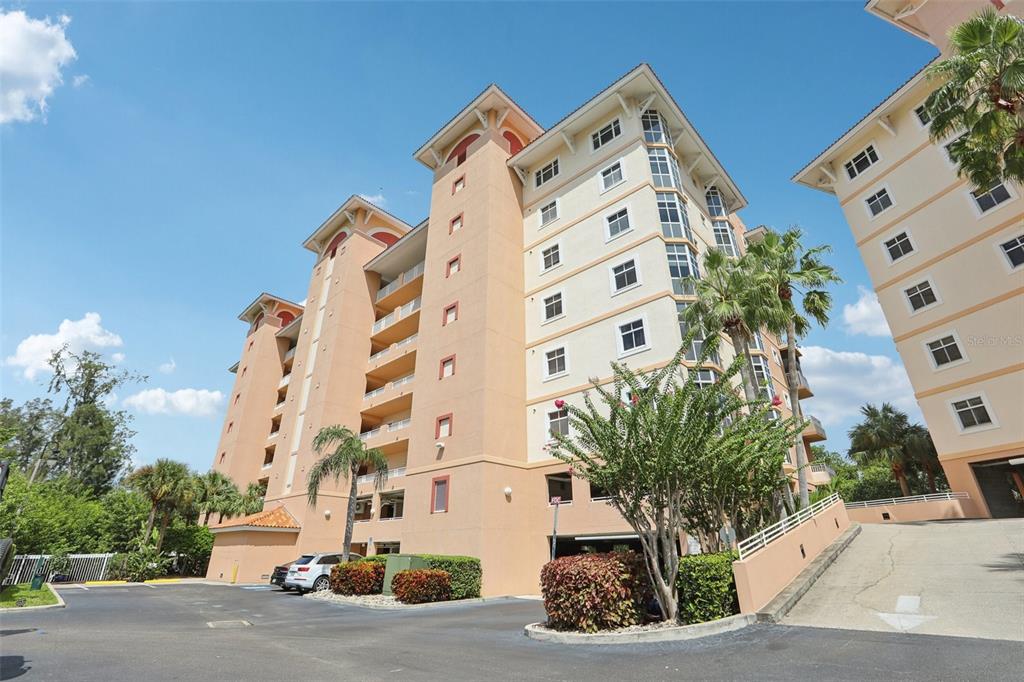 A multi-story tan apartment building with balconies and a parking area under a blue sky — 12033 GANDY BOULEVARD N UNIT 145, ST PETERSBURG, FL