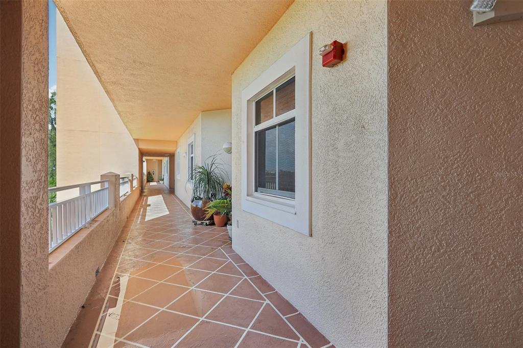An outdoor walkway with tiled flooring, a white railing, and a window on a stucco wall — 12033 GANDY BOULEVARD N UNIT 145, ST PETERSBURG, FL