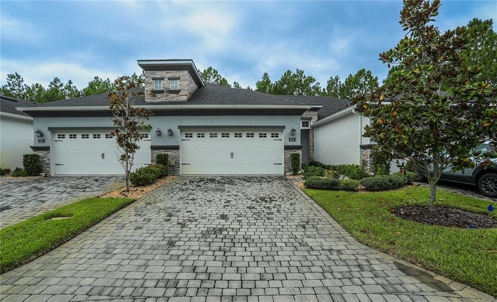 A two-car garage with a paver driveway and stone accents on a residential home exterior — 875 PINEWOOD DRIVE, ORMOND BEACH, FL