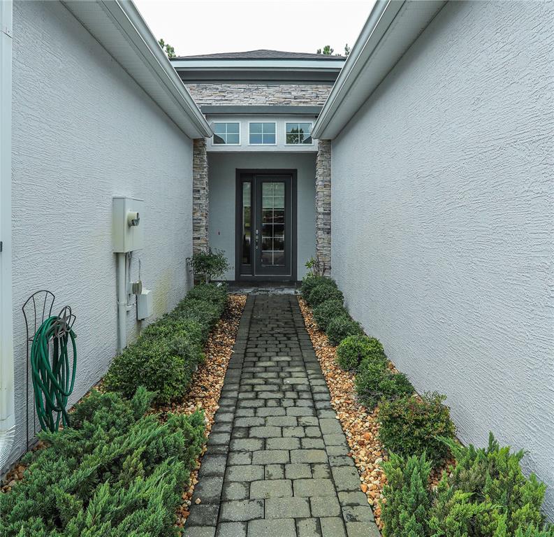 A stone paver walkway leads to a front door flanked by stone pillars and shrubs — 875 PINEWOOD DRIVE, ORMOND BEACH, FL