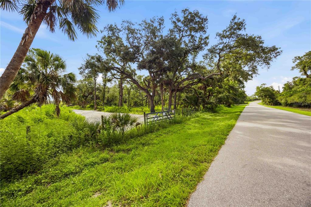 A paved road runs alongside a grassy lot with a gated entrance and large trees — S MOON DRIVE, VENICE, FL