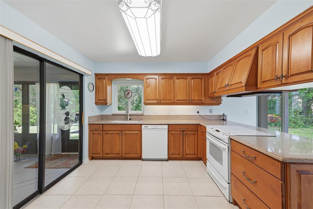 A kitchen features wood cabinets, granite countertops, white appliances, and a sliding glass door — 1803 NEW BEDFORD DRIVE, SUN CITY CENTER, FL
