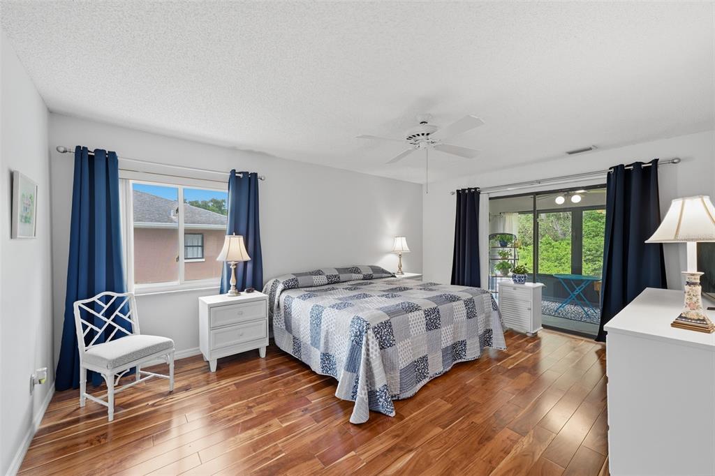 A bedroom features a bed with a blue quilt, hardwood floors, and sliding glass doors — 1803 NEW BEDFORD DRIVE, SUN CITY CENTER, FL