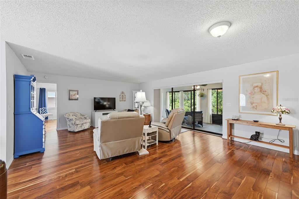 A living room features hardwood floors, a blue cabinet, and a sliding door to a patio — 1803 NEW BEDFORD DRIVE, SUN CITY CENTER, FL