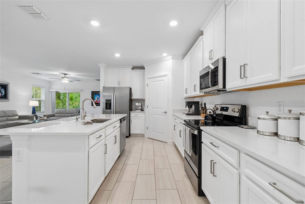 A modern white kitchen features a large island, stainless steel appliances, and light tile flooring — 16842 FORGE SURF STREET, LAND O LAKES, FL