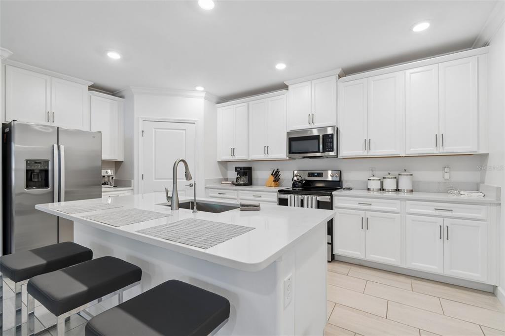 A modern kitchen features white cabinets, stainless steel appliances, a quartz island, and tile flooring — 16842 FORGE SURF STREET, LAND O LAKES, FL