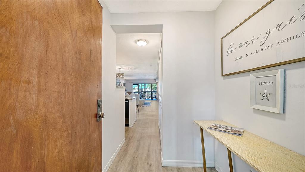 An entryway features light wood-look flooring, a console table, and wall art leading toward a living area — 1249 DOCKSIDE PLACE UNIT 110, SARASOTA, FL
