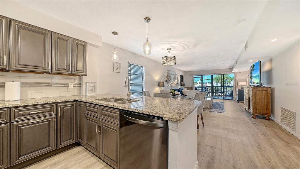 A kitchen with dark wood cabinets and granite countertops opens into a living area — 1249 DOCKSIDE PLACE UNIT 110, SARASOTA, FL