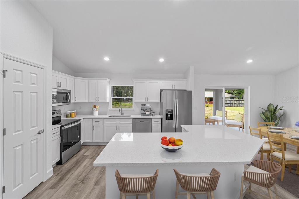 A modern kitchen features white cabinetry, stainless steel appliances, a quartz island, and wood-look flooring — 6283 NW 61ST STREET, OCALA, FL