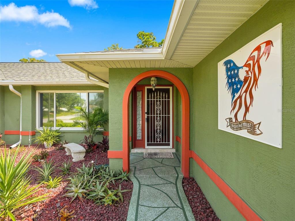 A green house exterior features a red-trimmed arched entryway and an American eagle wall art — 4382 MONTANO AVENUE, SPRING HILL, FL