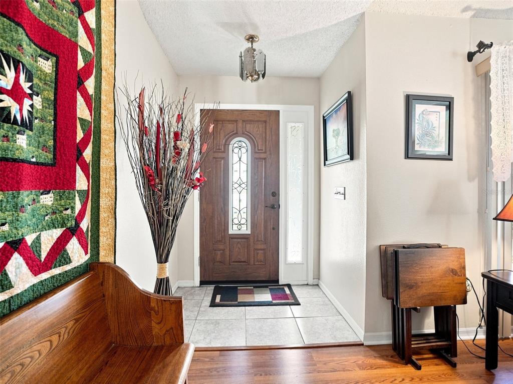 An entryway features a wooden front door, tiled floor, a wooden bench, and wall decor — 4382 MONTANO AVENUE, SPRING HILL, FL