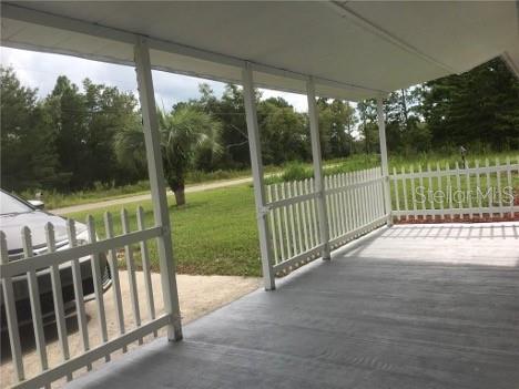 A covered porch with a white picket fence overlooks a grassy yard and a parked car — 22201 SW BEACH BOULEVARD, DUNNELLON, FL