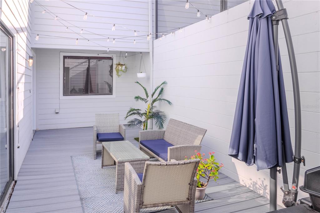 A patio features gray wicker furniture, a patterned rug, string lights, and a large umbrella — 3063 NW 28TH CIRCLE UNIT 3063, GAINESVILLE, FL