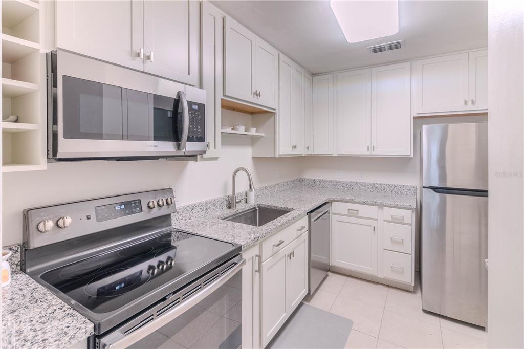 A kitchen features white cabinets, stainless steel appliances, and speckled granite countertops — 3063 NW 28TH CIRCLE UNIT 3063, GAINESVILLE, FL
