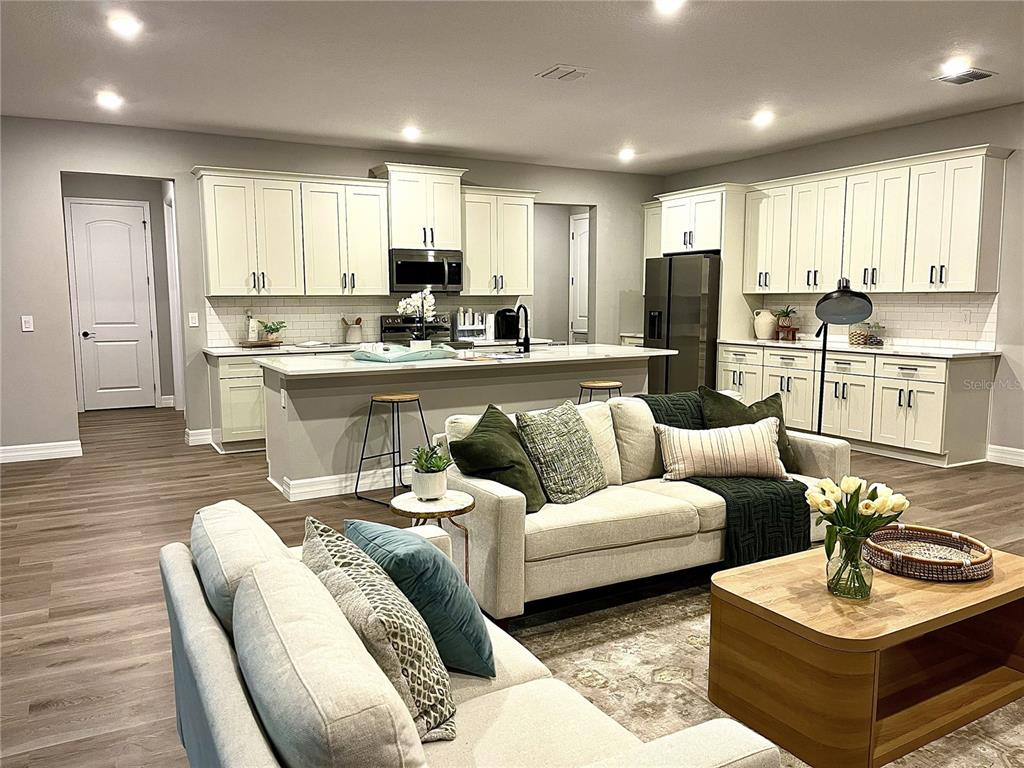 An open-concept kitchen and living area features white cabinetry, a central island, and neutral furniture — 7 LOBELIA COURT, HOMOSASSA, FL