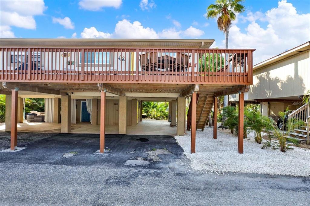 An elevated house with a large wooden deck, support pillars, and a covered ground-level area — 4909 GULF DRIVE UNIT 6B, HOLMES BEACH, FL