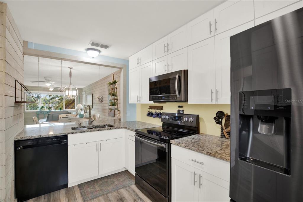 A kitchen features white cabinets, granite countertops, black appliances, and a view into the living area — 4909 GULF DRIVE UNIT 6B, HOLMES BEACH, FL