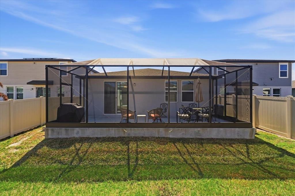 A screened-in patio with outdoor furniture sits behind a house with a fenced backyard — 1799 CARNOSTIE ROAD, WINTER HAVEN, FL