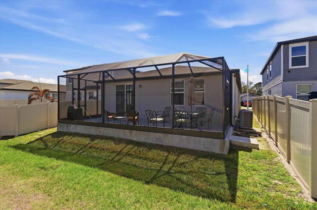 A screened-in patio with outdoor furniture sits behind a house with a vinyl fence — 1799 CARNOSTIE ROAD, WINTER HAVEN, FL