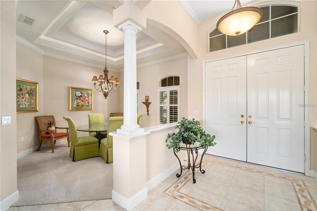 A foyer with tile flooring leads to a carpeted dining area featuring a glass table — 1023 RAINBOW COURT, BRADENTON, FL