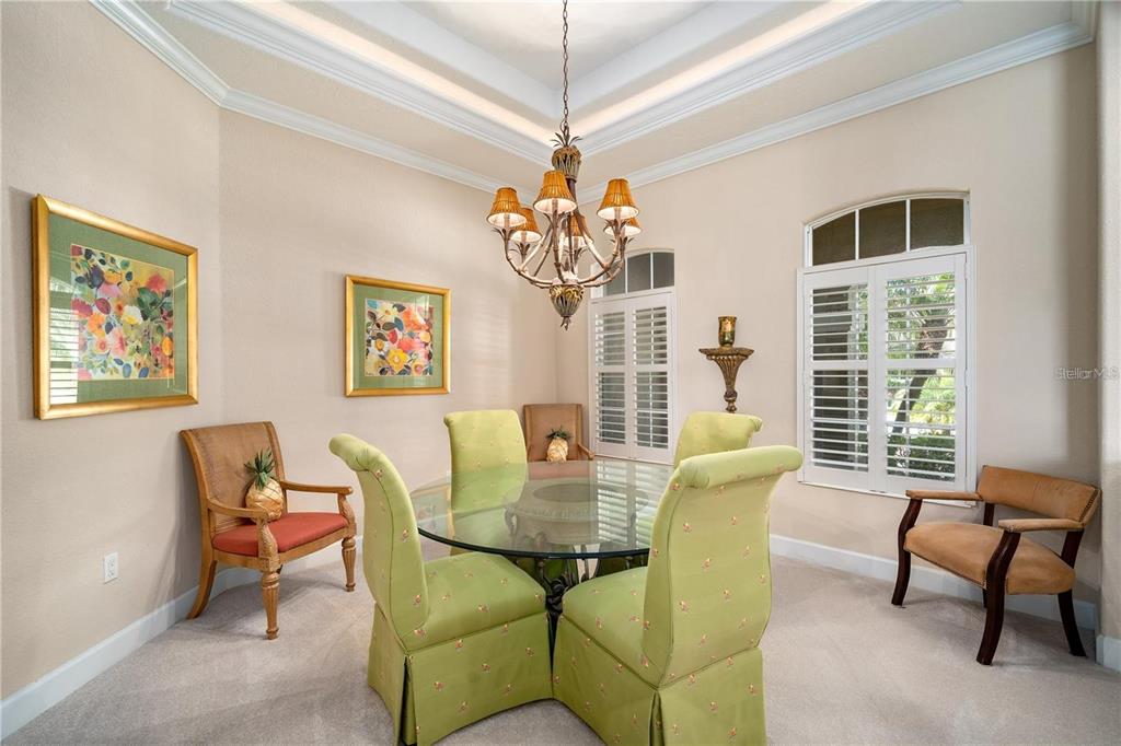 A dining room features a glass table, green upholstered chairs, a chandelier, and plantation shutters — 1023 RAINBOW COURT, BRADENTON, FL
