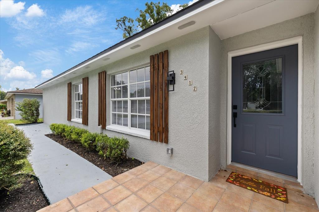 A gray house exterior features a blue front door, wood shutters, and a tiled porch — 3417 LORI LANE S, LAKELAND, FL