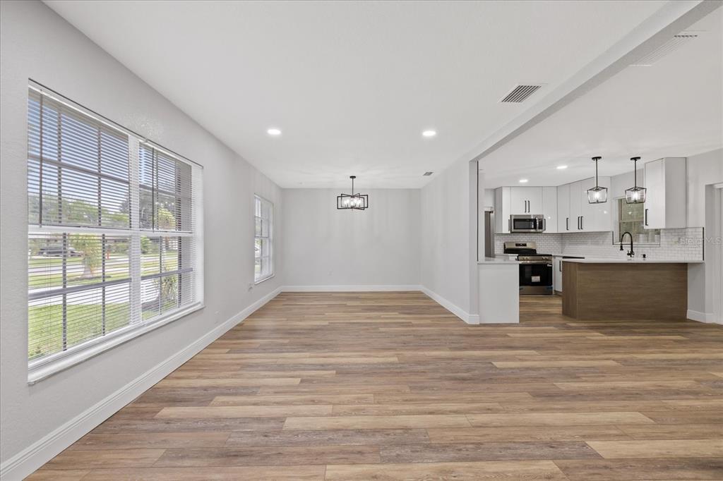 An open-concept dining area with wood-look flooring leads into a modern kitchen with white cabinets — 3417 LORI LANE S, LAKELAND, FL