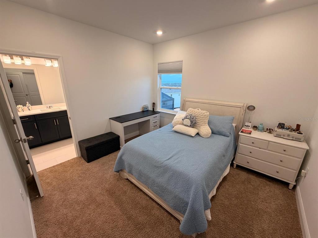 A bedroom with a bed, desk, dresser, and an attached bathroom with dark cabinets — 1656 PYRAMID HILL STREET, MINNEOLA, FL