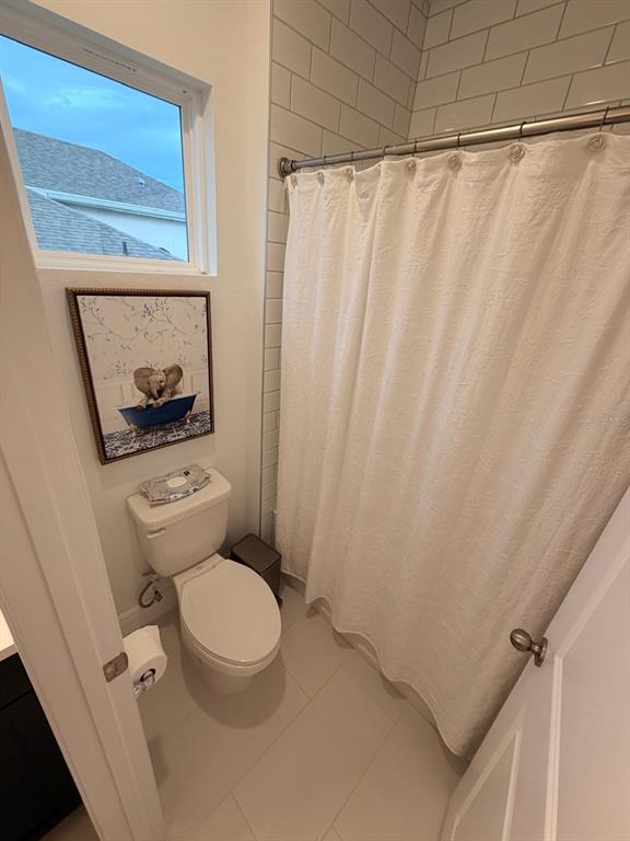 A bathroom features a white toilet, a shower with a white curtain, and framed wall art — 1656 PYRAMID HILL STREET, MINNEOLA, FL